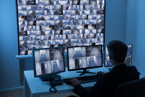 Ein Mann sitzt vor einer Leinwand mit zahlreichen Kamerabildern zur Videoüberwachung